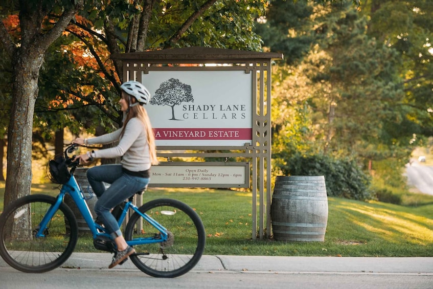 A person riding a bicycle past a sign for Shady Lane Cellars, a vineyard estate. 3