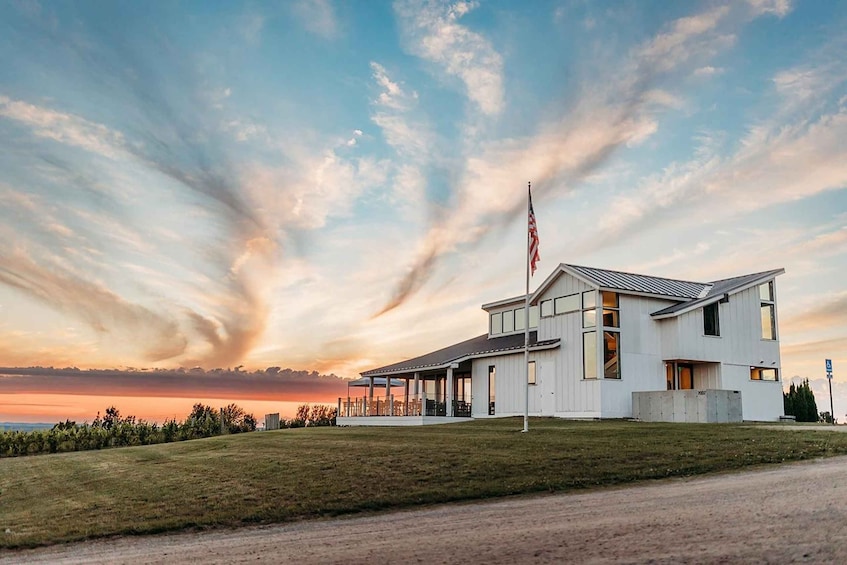 A modern two-story house with a covered porch, a flagpole with an American flag, and a sunset sky with clouds. 1