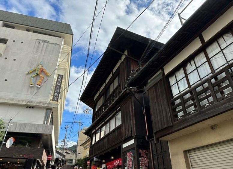 A street with buildings, including a two-story wooden structure and a modern building with a mannequin on the roof. 2