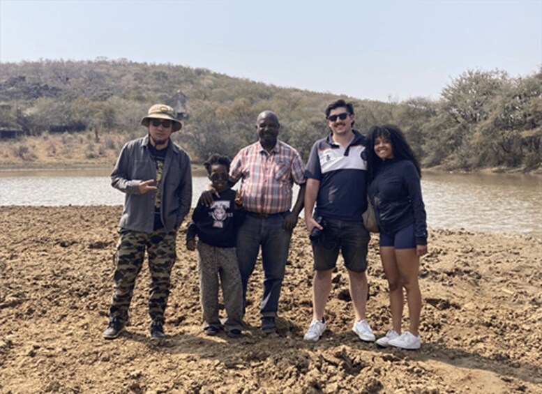 A group of people standing on a sandy beach with a river and hills in the background. 3