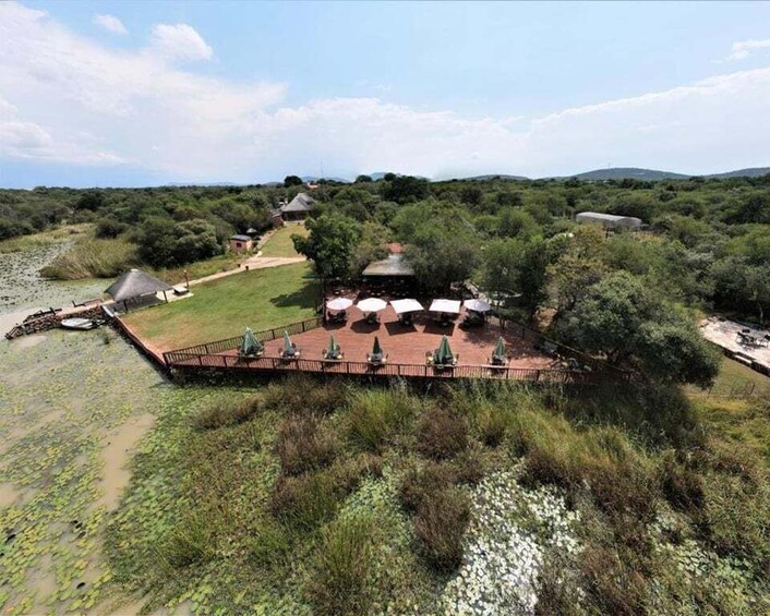 A riverside lodge with a thatched-roof structure, surrounded by lush greenery and a clear sky. 5