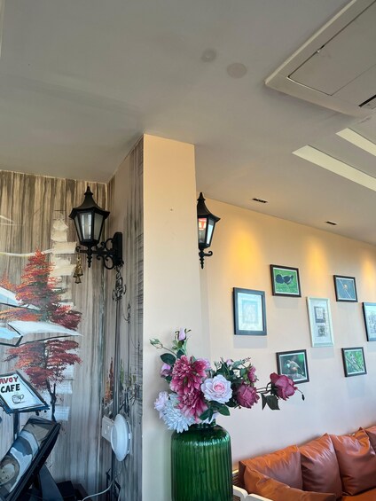 A room with a green vase of flowers, a sofa, wall-mounted picture frames, and a mural with a tree and cafe sign. 2