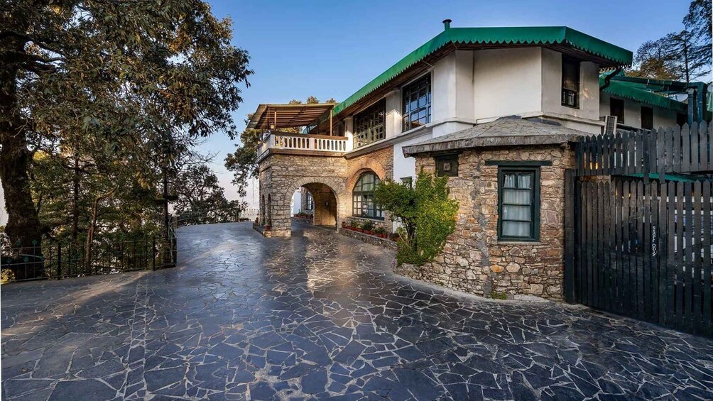 A stone house with a green roof, a paved driveway, and a metal gate. 1