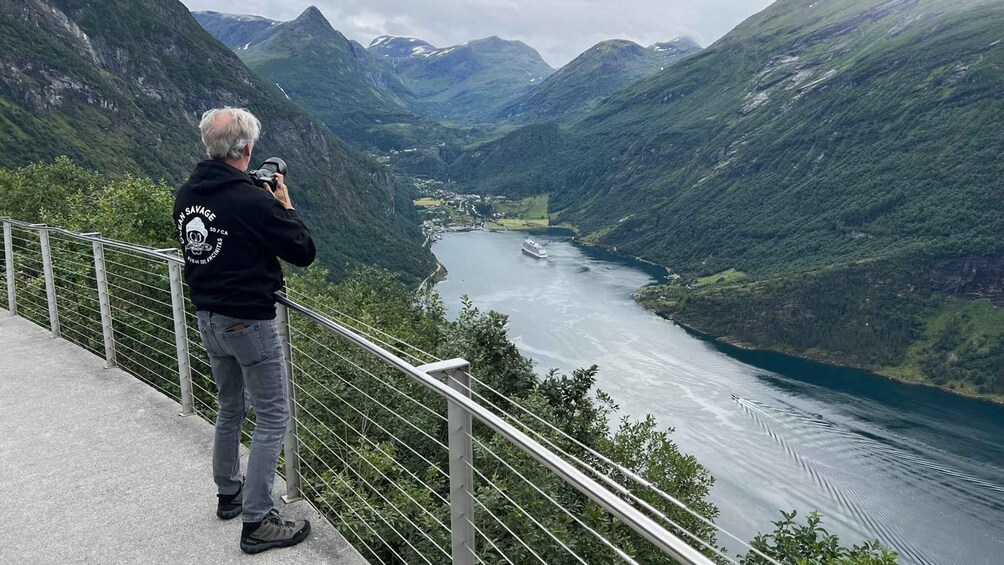 A person taking a photo of a river with mountains in the background. 4