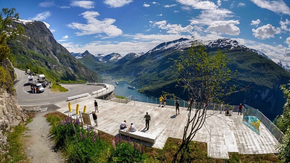 A mountainous landscape with a winding road, a viewing platform, and a body of water. 1