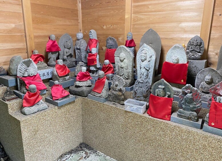 A collection of stone statues, some with red cloths, displayed in a wooden structure. 5