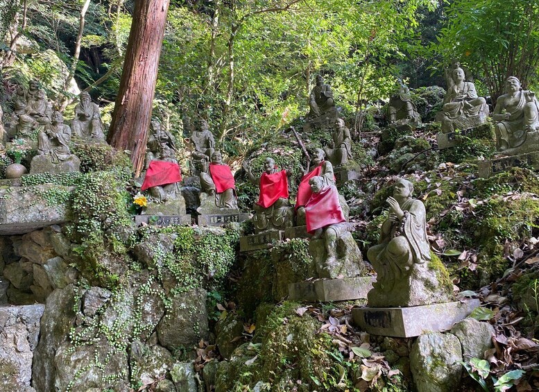 A collection of stone statues in a forested area, some with red cloths. 2