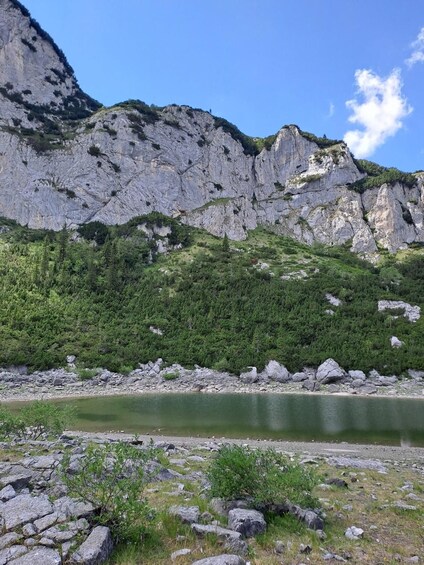 A mountainous landscape with a calm lake, rocky shore, and dense green forest. 2