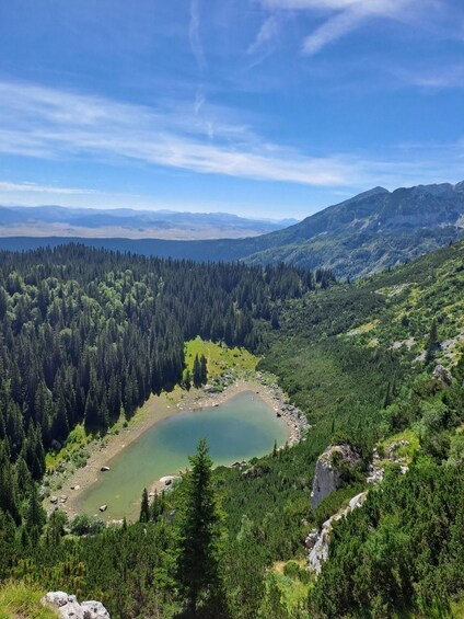 A mountainous landscape with a lake surrounded by dense forests and distant mountain ranges. 1