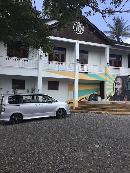 A building with a mural, a parked car, and a staircase leading to the entrance. 5
