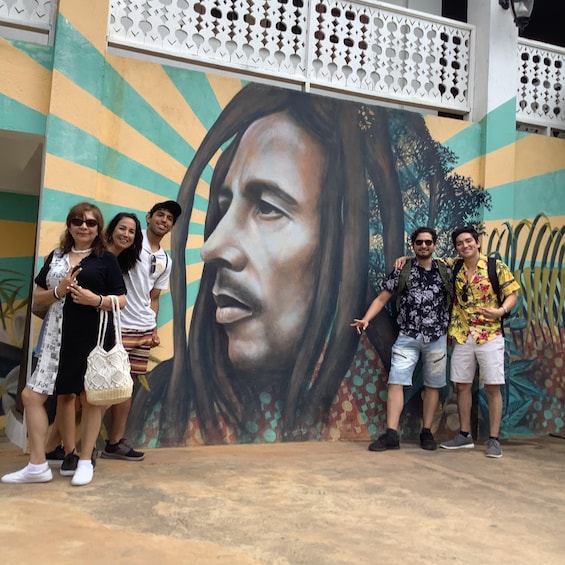 A mural with a large portrait of a person, a decorative white lattice structure, and a group of people posing in front of it. 1