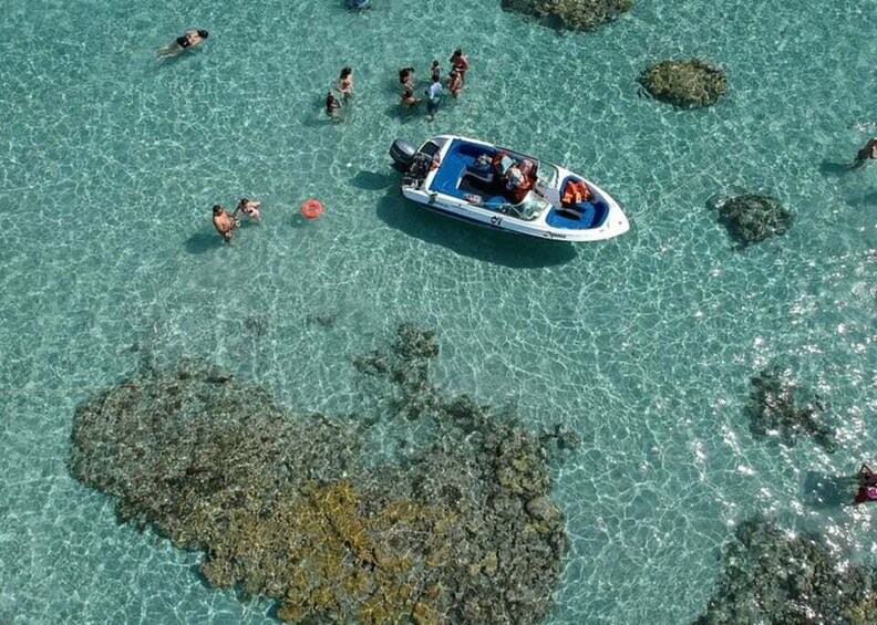 A boat with people on a clear blue sea with rocky formations. 2