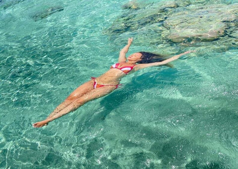 A person floating on a clear blue body of water with rocks visible beneath the surface. 3