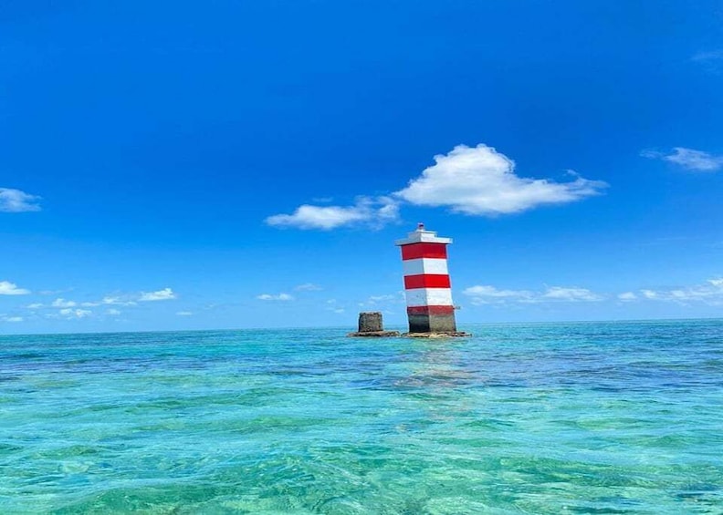A lighthouse with red and white stripes, surrounded by clear turquoise water and a blue sky with clouds. 4