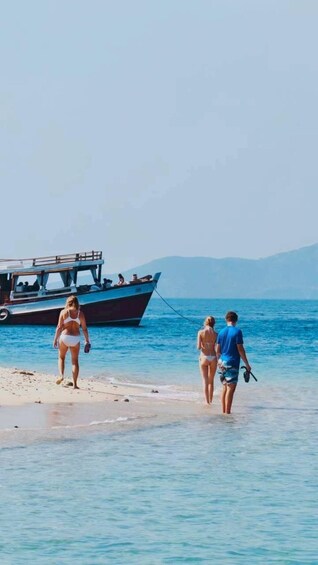 A beach with clear blue water, a boat, and people walking along the shore. 1