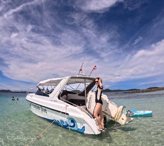 A boat named Freedom Dive with a person on board, anchored in clear water with a rocky shoreline in the background. 4
