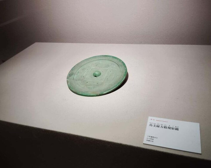 A green ceramic object with a central hole, displayed on a white pedestal with a label. 2