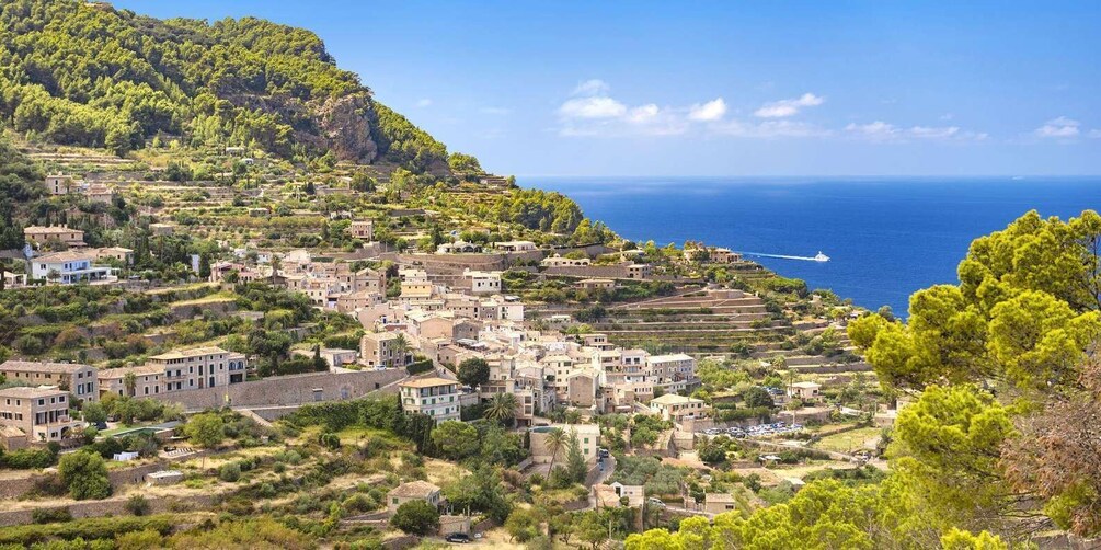 A coastal village with terraced houses, a clear blue sea, and a boat in the distance. 1
