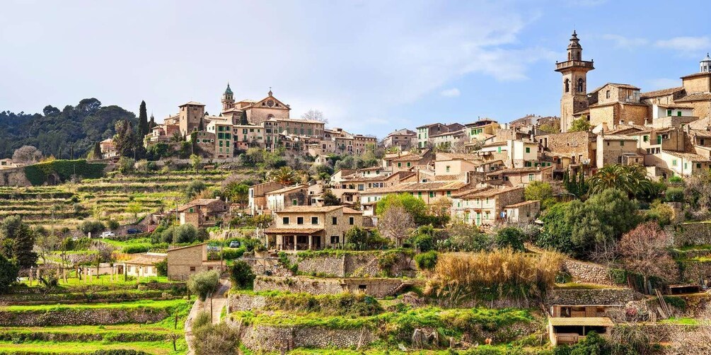 A hillside village with terraced fields, historic buildings, and a prominent church with a bell tower. 3