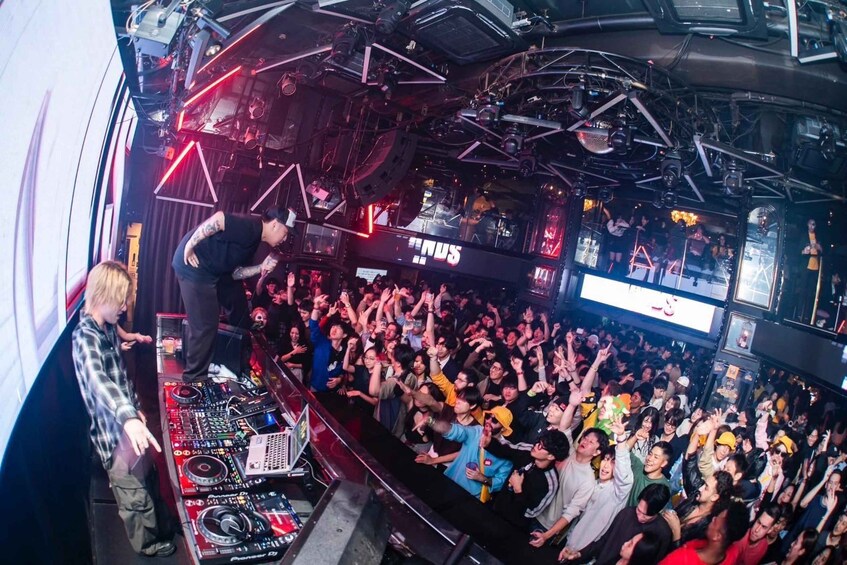 A crowded nightclub with a DJ booth and a large crowd. 1