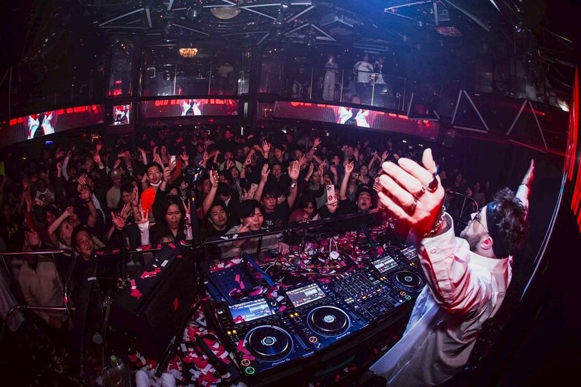 A crowded nightclub with a DJ booth and a large audience. 2