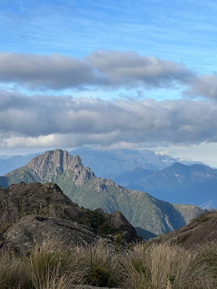 A mountainous landscape with a prominent rocky peak in the foreground and a range of mountains in the background under a partly cloudy sky. 4