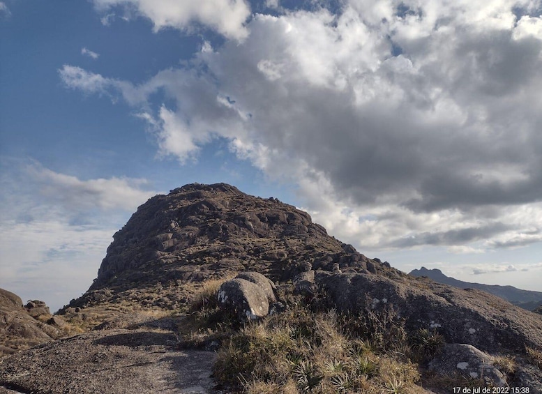 A rocky mountain landscape with sparse vegetation and a clear sky with clouds. 1