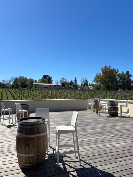 A wooden deck with white chairs and barrels, overlooking a vineyard. 2