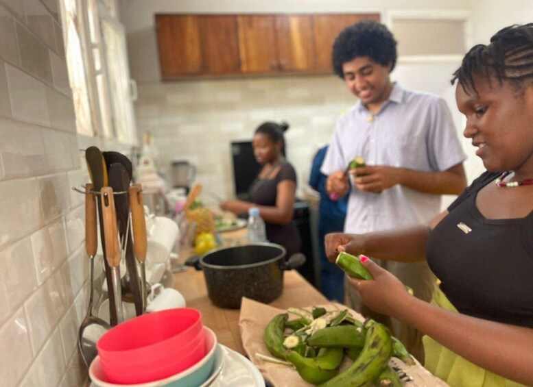 A kitchen with people preparing food, a red bowl, a pot, and kitchen utensils. 1