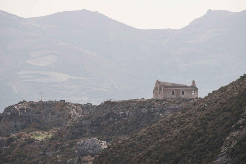A solitary building on a hilltop with a mountainous backdrop. 1