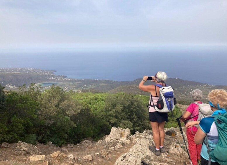 A group of hikers on a rocky outcrop overlooking a coastal landscape with a view of the sea and distant buildings. 5