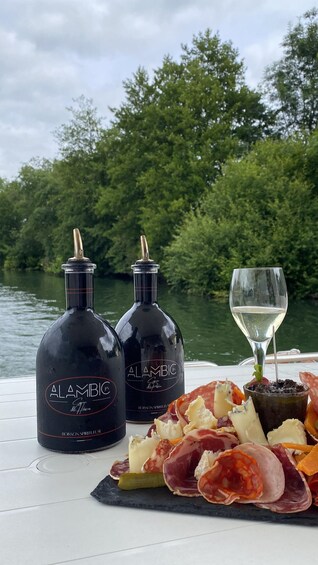 Two bottles of Alambic Cognac, a glass of white wine, and a charcuterie board with various meats and cheeses on a boat. 4