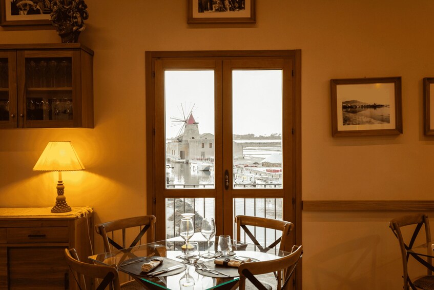 A dining area with a table set for four, a lamp, and a view of a windmill through a glass door. 1