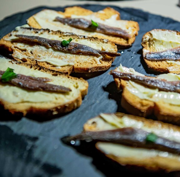 Slices of bread topped with cheese and anchovies arranged on a dark slate plate. 4