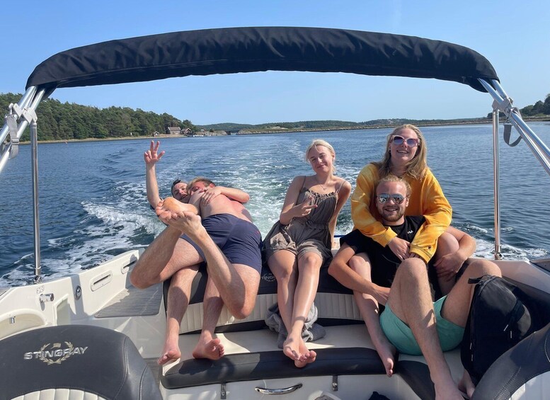 A group of people on a boat with a canopy, water, and a forested shoreline in the background. 1