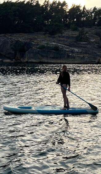 A person paddleboarding on a calm body of water with a rocky shoreline and trees in the background. 2