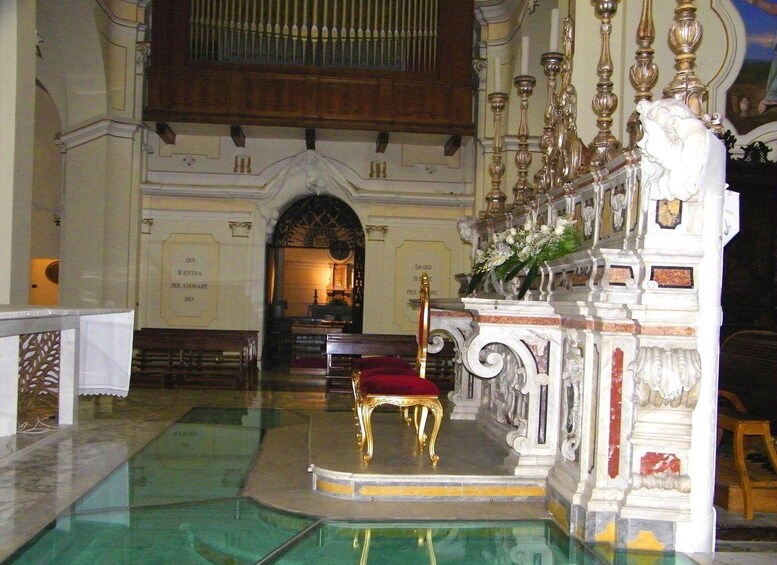 An ornate church interior with a golden chair, a marble floor, and a large organ. 1