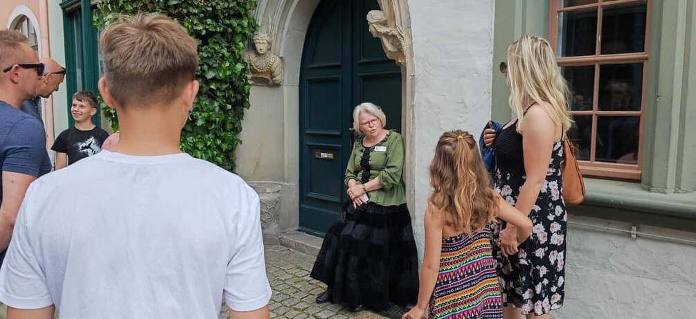 A group of people standing outside a building with a green door and a stone statue. 4