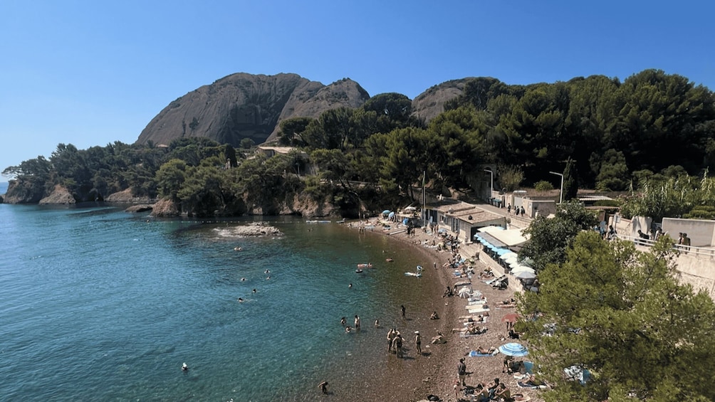 A coastal beach with clear water, people swimming and sunbathing, and a mountainous backdrop. 1