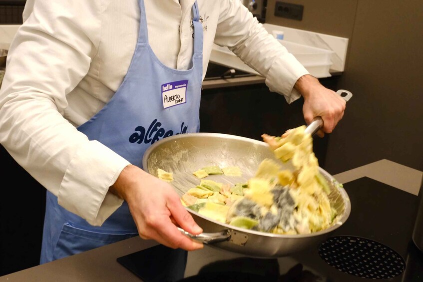 A person in a chef's uniform with a name tag, stirring a mixture in a large metal pan. 5