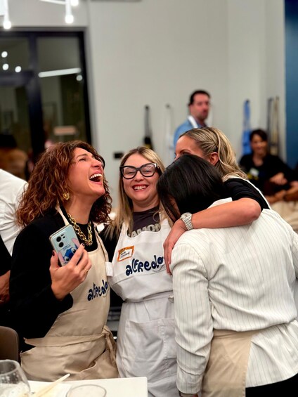 A group of people wearing aprons, some with 'alcredo' printed on them, gathered in a room with tables and chairs. 2