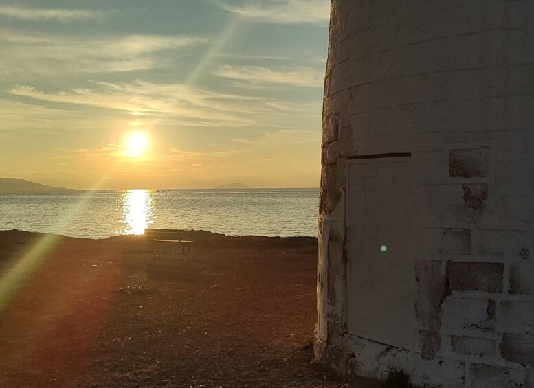 A sunset over a body of water with a bench and a weathered building. 1