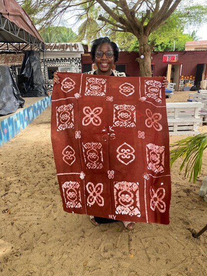 A person holding a patterned cloth outdoors with a stage and trees in the background. 3