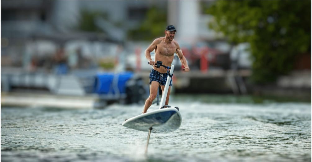 A person windsurfing on a body of water with a blurred background of buildings and trees. 3