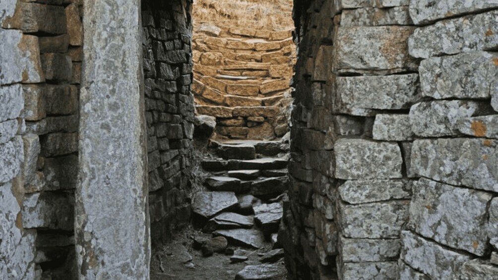 A narrow stone passageway with a rough stone wall on one side and a smoother stone wall on the other. 5