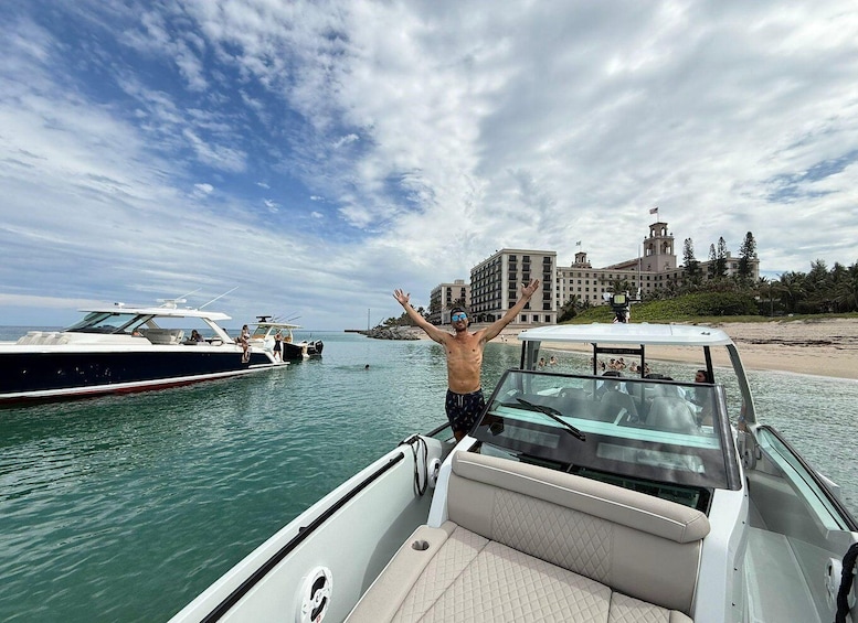 A man on a boat with arms raised, a large building with a tower in the background, and a clear sky. 3