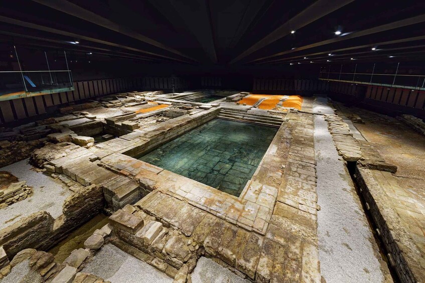 An ancient archaeological site with stone structures and a central pool. 4