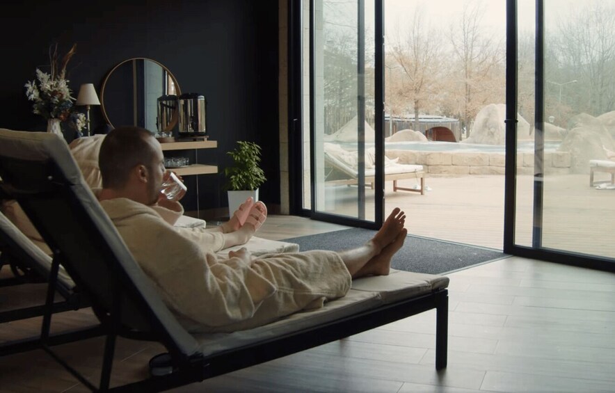 A person reclining on a lounge chair indoors with a view of an outdoor swimming pool area. 3