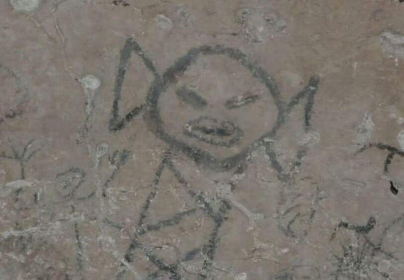 A stone wall with ancient carvings of a figure with pointed ears and a triangular nose. 2
