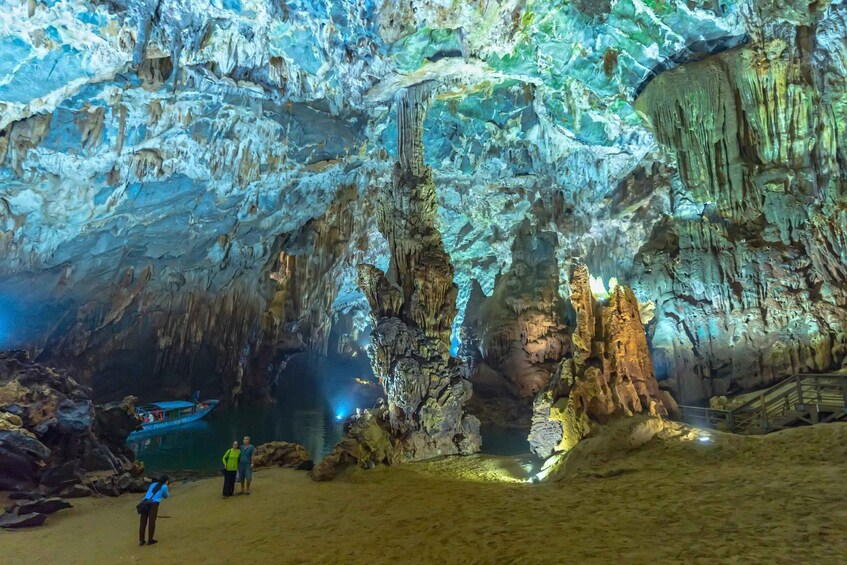 A cave with stalactites and stalagmites, a boat on the water, and people exploring. 2